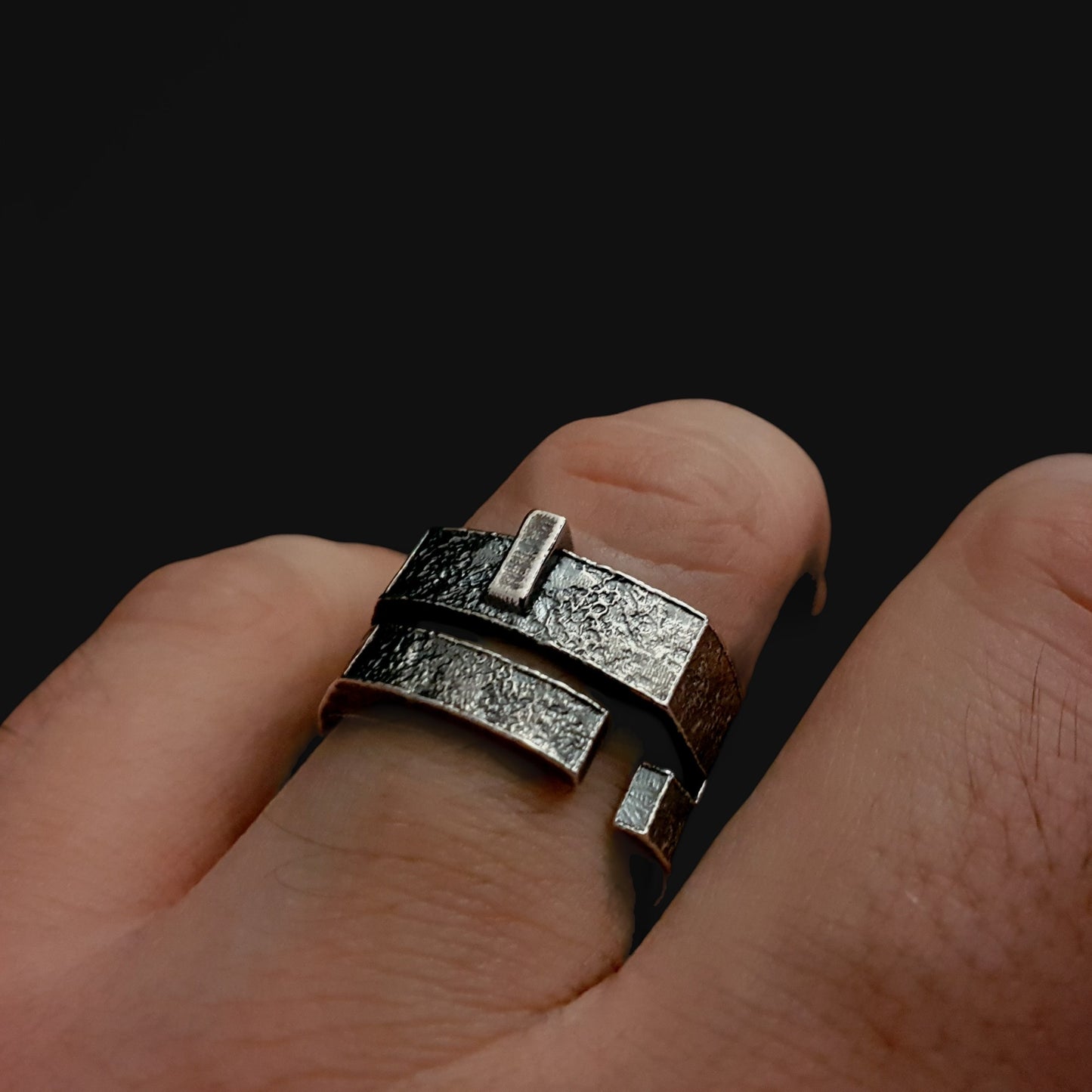 brutalist Silver ring with a unique design worn on a finger against a black background