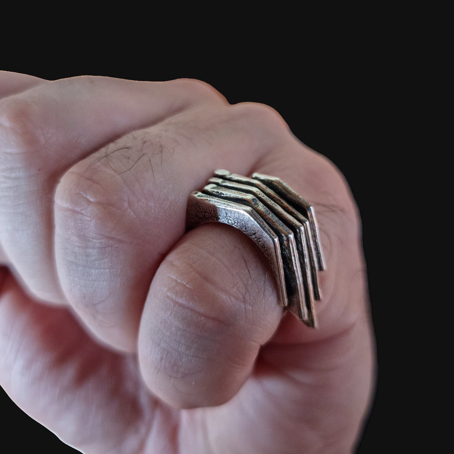 Hand wearing a unique silver ring with geometric design on a black background