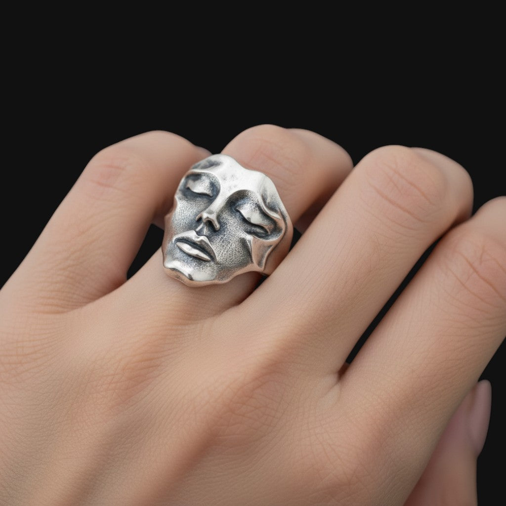 Brutalist Silver face-shaped ring on a hand against a black background